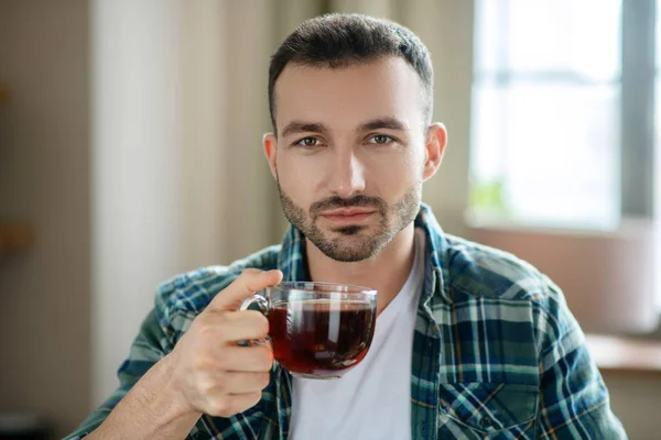 Young man in a checkered shirt having tea — Stock Photo, Image