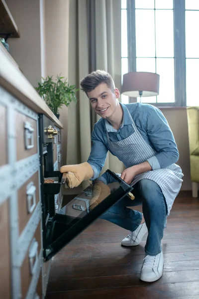 Sonriente joven sacando una bandeja para hornear del horno . — Foto de Stock