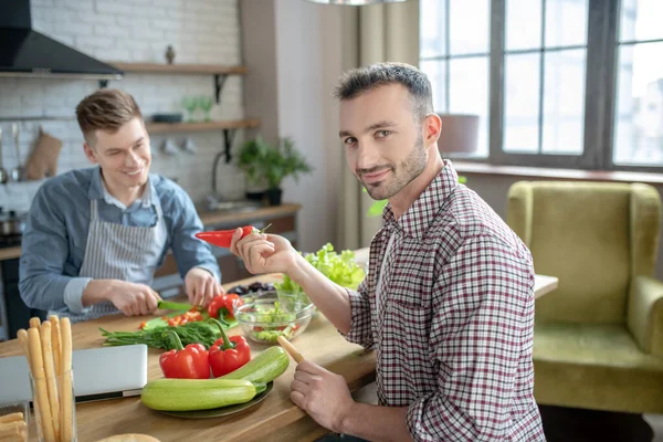 Pareja masculina sentada a la mesa preparando comida vegetariana . — Foto de Stock