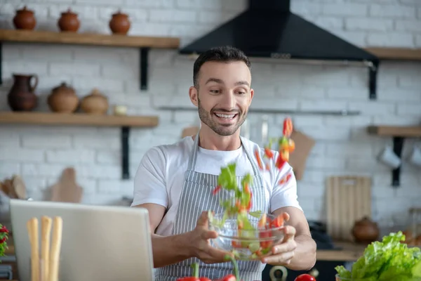 Dark-haired man with a bowl in his hands tossing chopped vegetables. — Stockfoto