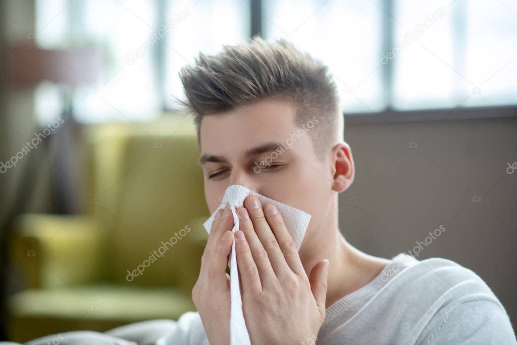 Fair-haired young man looking sick and sneezing