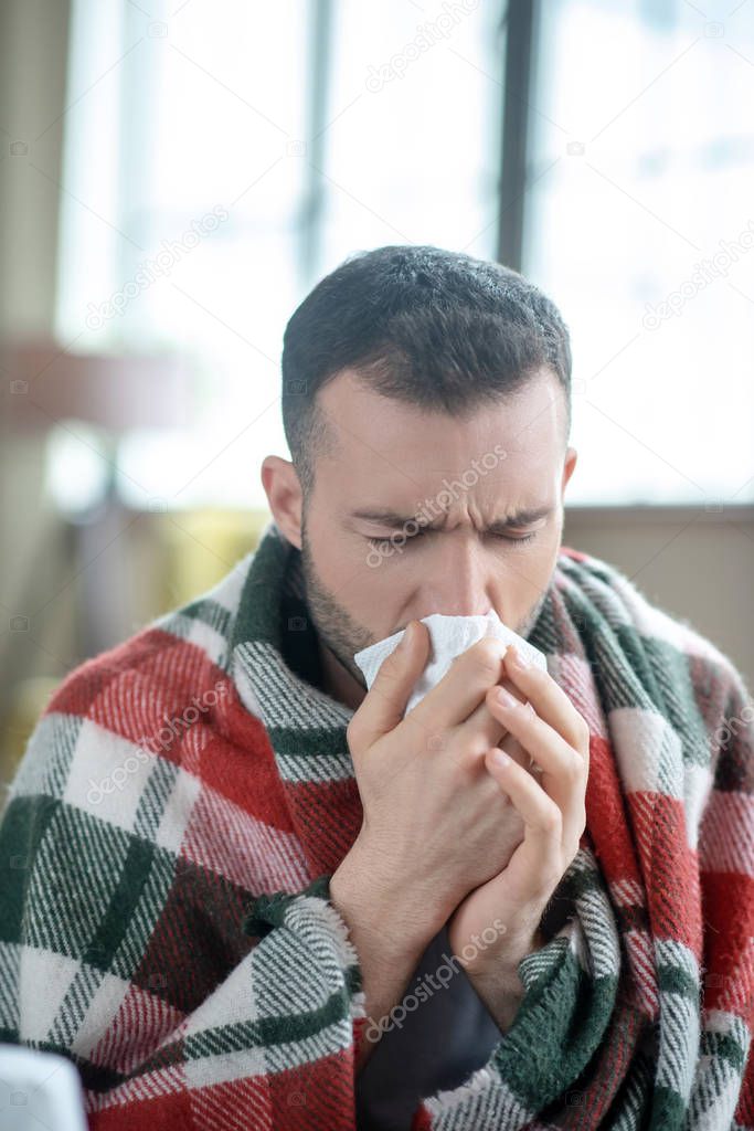 Dark-haired young sick man sneezing and feeling unwell
