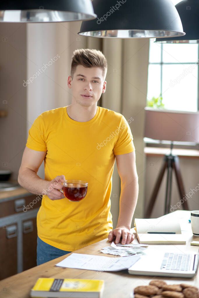 Young fair-haired man in yellow tshirt standing near the table