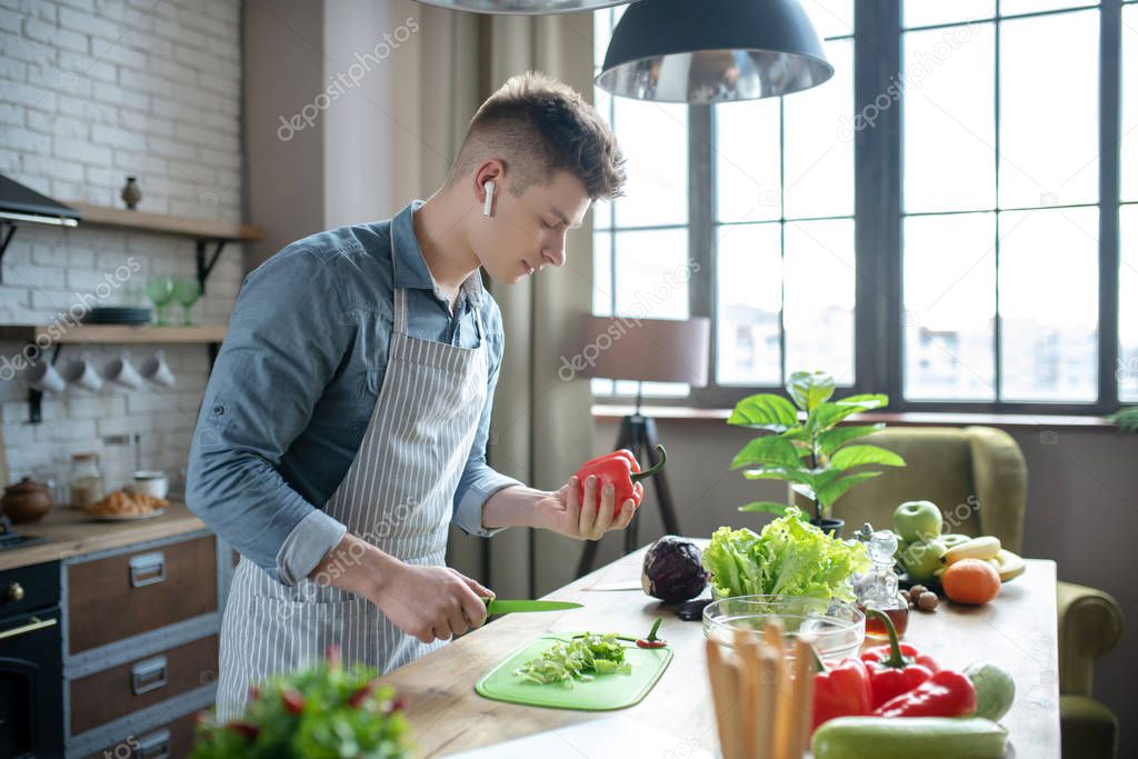 Young successful man slicing fresh vegetables in the kitchen.