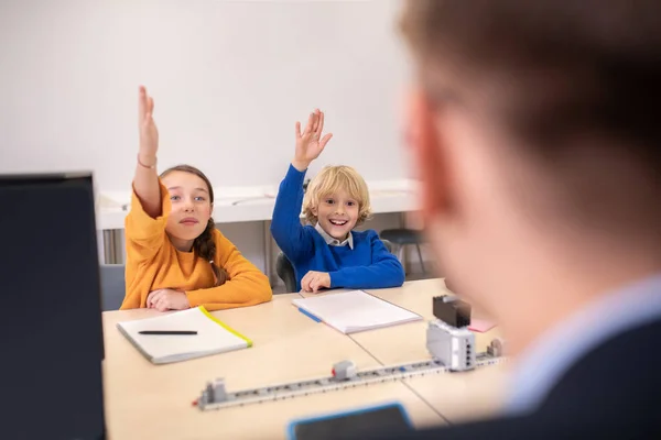 Учні сидять за столом, піднімаючи руки — стокове фото