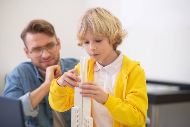 Çocuk engelleri takıyor, öğretmen ona bakıyor.