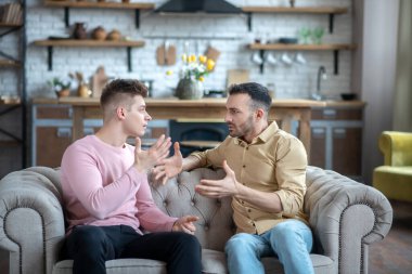 İki adam kanepede oturmuş tartışıyor.