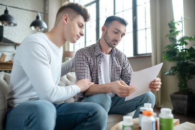 Kareli gömlekli sakallı genç adam test sonuçlarını okuyor.