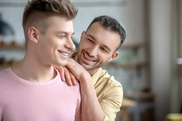 Donkerharige man in oranje shirt legt handen op zijn partners schouder — Stockfoto