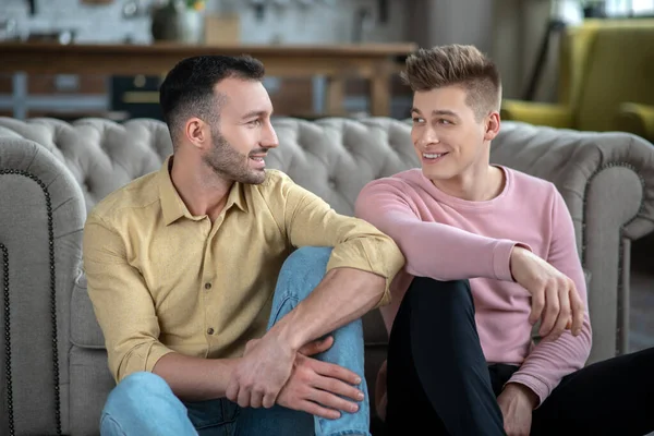 Gay casal sentado no o chão sorrindo e olhando para o outros — Fotografia de Stock