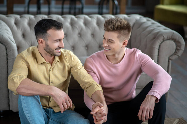 Gay couple sitting on the floor holding each others hands