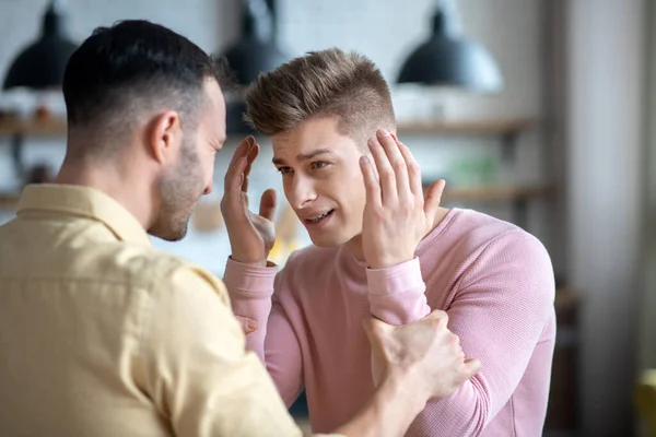 Hombre barbudo de pelo oscuro sosteniendo los brazos de sus compañeros que parecen enojados — Foto de Stock