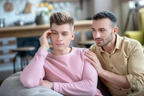 Homme en chemise rose assis sur le canapé se sentant contrarié et offensé — Photo