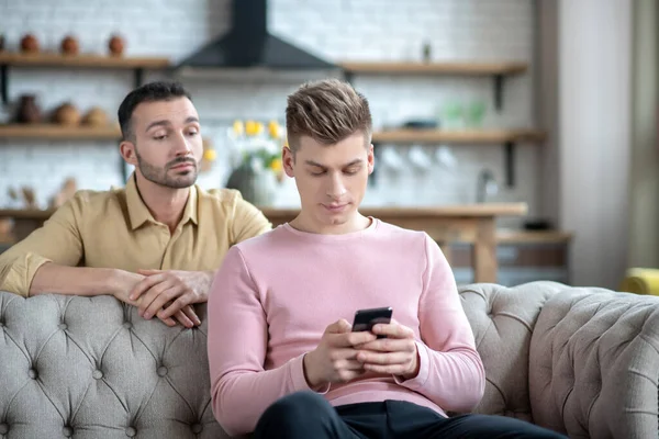 Man in orange shirt watching his partner chatting online — Stock Photo, Image