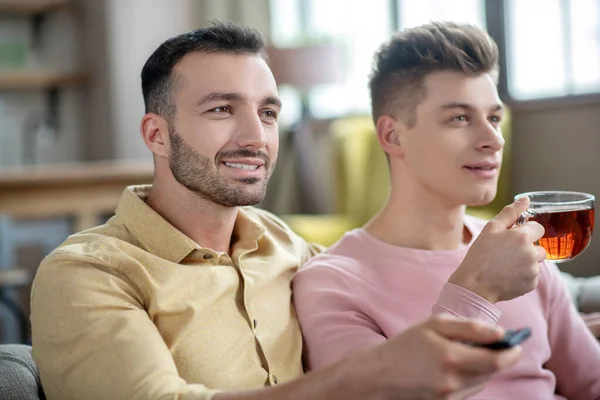 Due giovani uomini che prendono il tè e guardano la tv insieme — Foto Stock