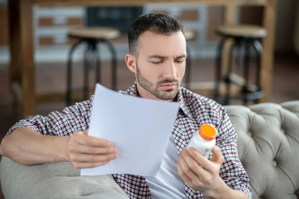 Joven con camisa a cuadros leyendo prescripción y mirando atento — Foto de Stock