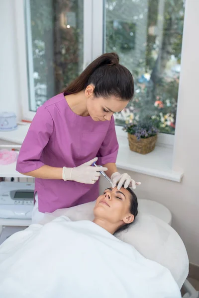 Cosmetólogo vistiendo uniforme morado haciendo inyecciones de belleza — Foto de Stock