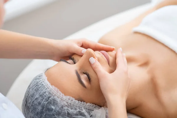 Médico de belleza haciendo masaje facial para el cliente mintiendo y disfrutando — Foto de Stock