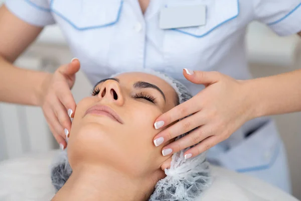 Kosmetický lékař dělá masáž obličeje pro klienta lhaní a těší — Stock fotografie