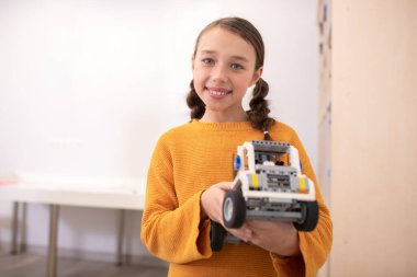 Koyu renk saçlı kız, elinde araba, mutlu bir şekilde gülümsüyor.