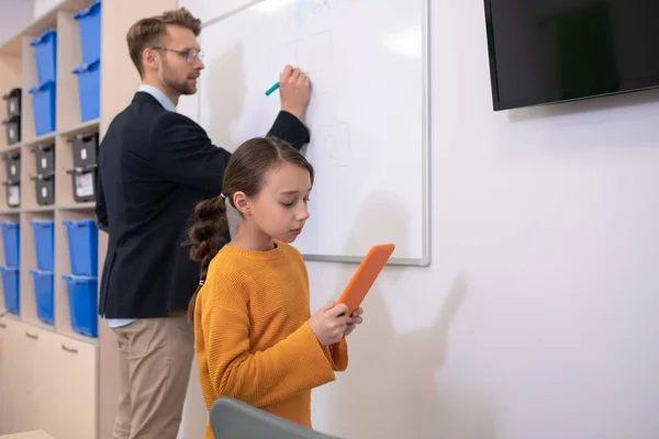 Man leraar schrijven op whiteboard, meisje iets te lezen op tablet — Stockfoto