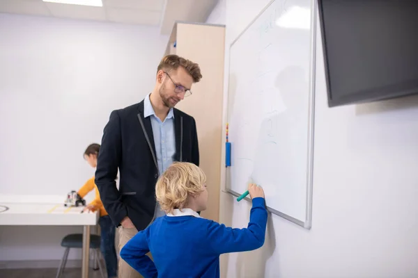 Erkek öğretmen tahtada duruyor, çocuk yazıyor. — Stok fotoğraf