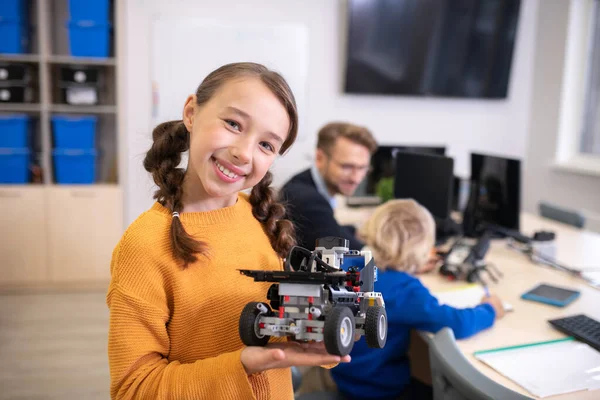 Lány gazdaság építhető autó és mosolygós, tanár és fiú a háttérben — Stock Fotó