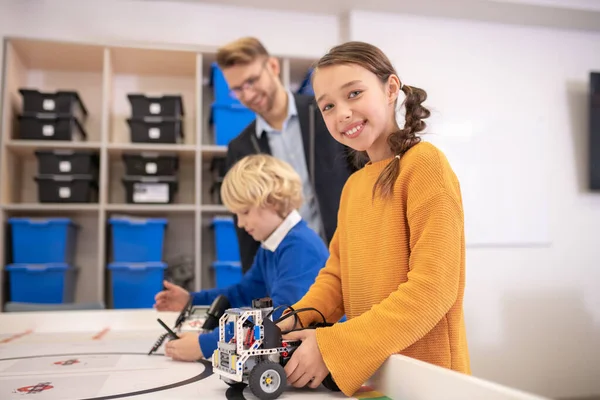 Menina de cabelos escuros segurando carro construível, menino brincando com o seu, professor observando-os — Fotografia de Stock