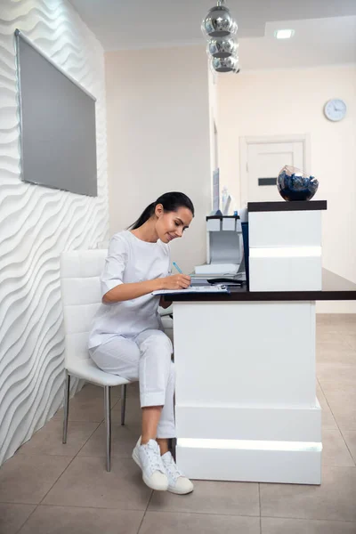 Recepcionista con uniforme blanco y zapatillas de deporte haciendo notas — Foto de Stock