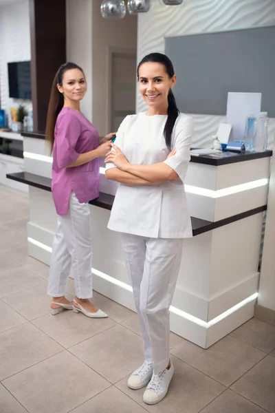 Cheerful worker of beauty clinic wearing white uniform and sneakers — Stock Photo, Image