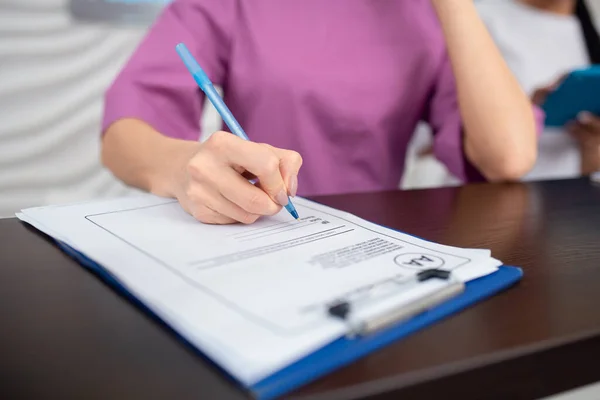 Receptioniste draagt paars uniform met pen terwijl ze aantekeningen maakt — Stockfoto