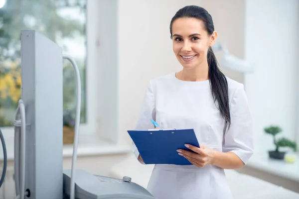 Cirujano plástico sonriendo mientras toma notas después de la cita —  Fotos de Stock