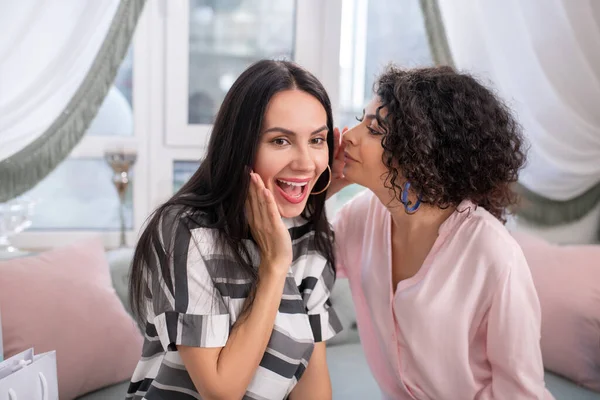 Two dark-haired women sitting on the sofa and sharing secrets — 스톡 사진