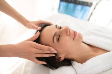 Dark-haired woman feeling relaxed while having facial massage