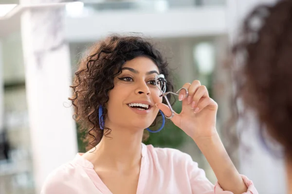 Morena sonriente mujer rizando sus pestañas con un rizador — Foto de Stock