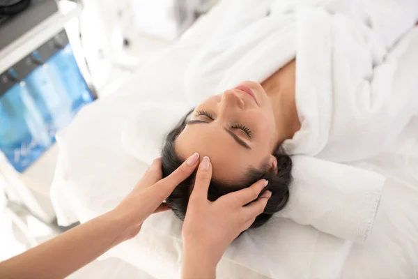 Mujer de cabello oscuro acostada en el sofá teniendo masaje facial —  Fotos de Stock