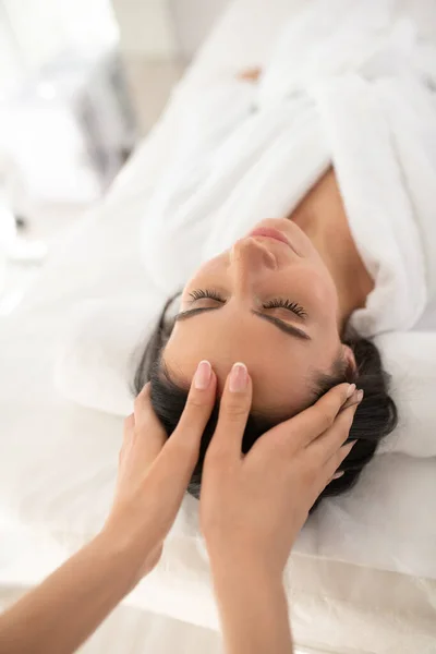 Dark-haired woman lin a white robe having face massage — Stockfoto