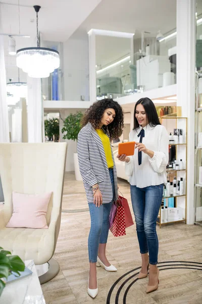 Beauty shop assistant in a white blouse showing products to a new visitor — Stockfoto