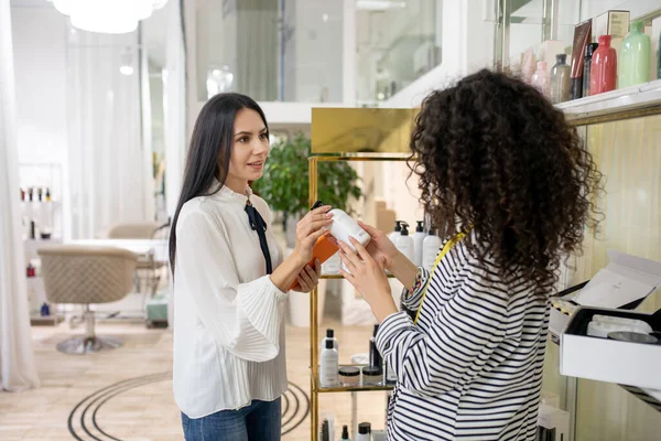 Dark-haired woman in a striped jacket asking about price of body lotion — Stok fotoğraf