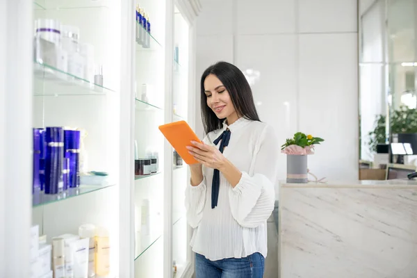 Bastante consultor de belleza en una blusa blanca comprobando información en línea — Foto de Stock