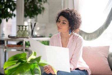 Beautiful curly-haired woman holding price list in her hands
