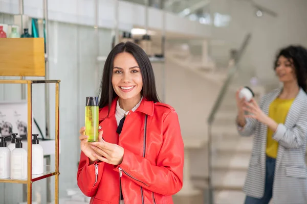 Brunette woman in a red jacket choosing a shower gel — Stok fotoğraf