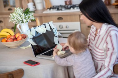 Young mom and daughter sitting at laptop, typing, playing