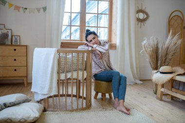 Tired mom sitting at the cot, resting her head on hands
