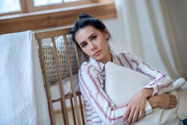 Sad young woman hugging pillow, leaning on cot