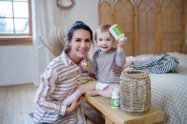 Mom and daughter sitting together, girl holding bottle with bandage on her leg