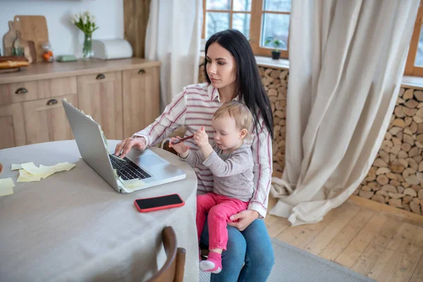 Mom working at laptop, holding her daughter — Stockfoto