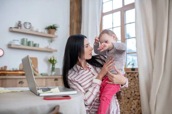 Young mom holding baby, distracted from work — Stockfoto