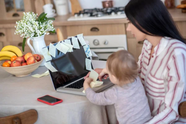 Young mom and daughter sitting at laptop, typing, playing — Stockfoto