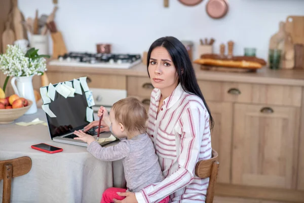 Stressed mom sitting with daughter, trying to manage her work — Stockfoto